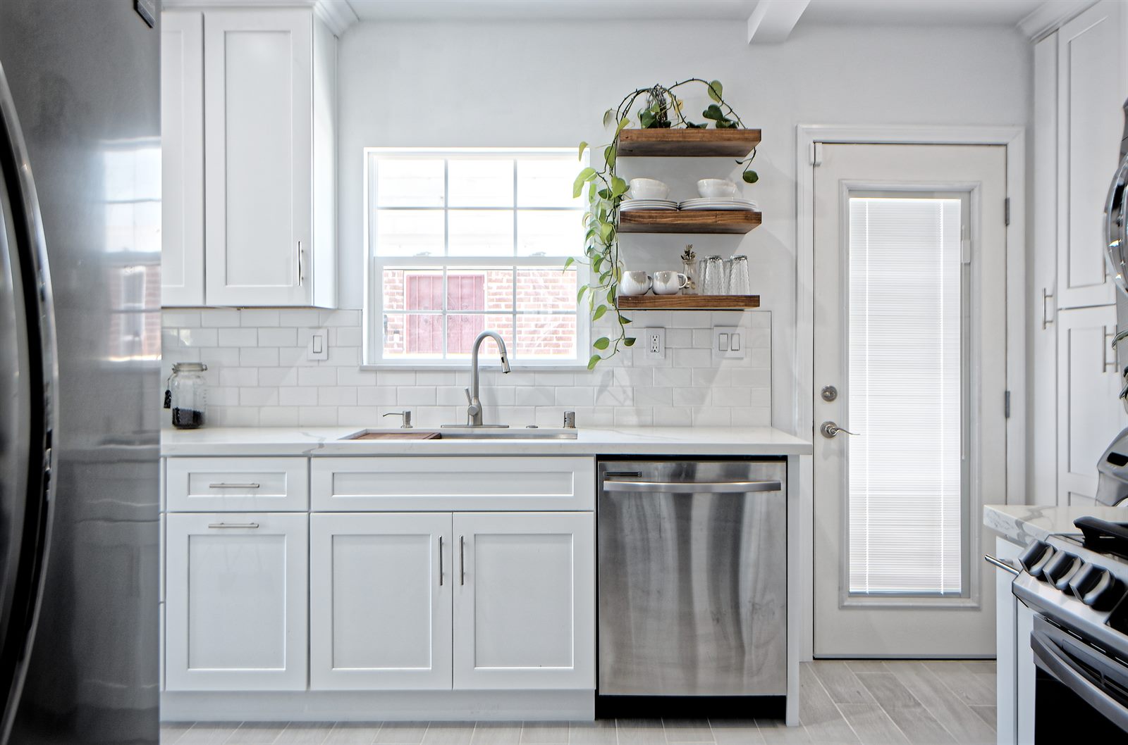 After: white shaker kitchen with open wood shelves, sink view