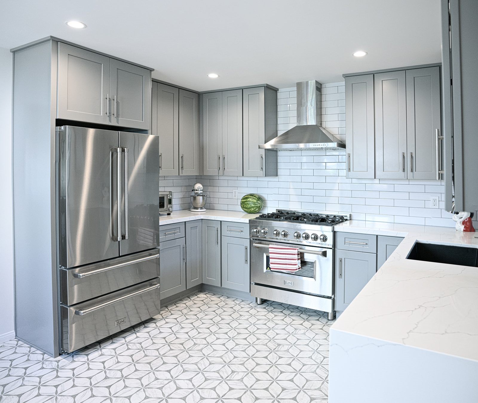 After: gray shaker kitchen close-up showing range, vent hood, fridge, and patterned floor tile