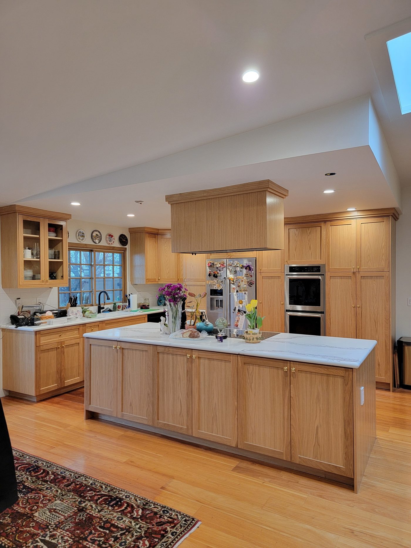 After: natural wood kitchen showing large marble island, double oven, and skylight